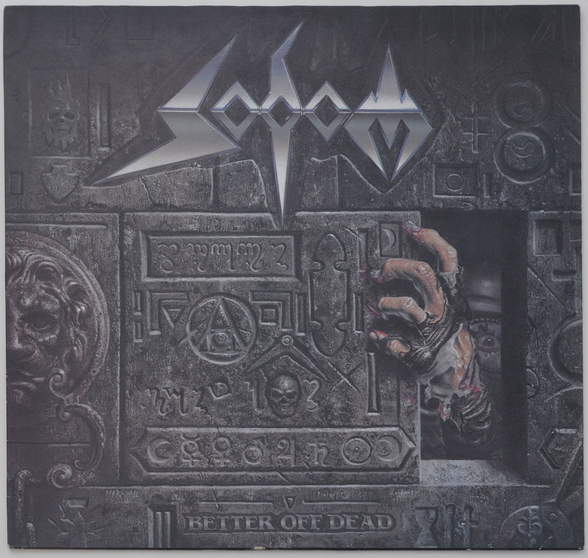 Album cover for Sodom’s Better Off Dead featuring a dark stone wall with engraved symbols, a skeletal hand reaching out from an opening, and a single eye peering from the shadows
